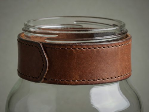 Soft-lit 3D render showing how a stitched vegetable-tanned leather cuff hides the螺旋 screw thread of a glass jar